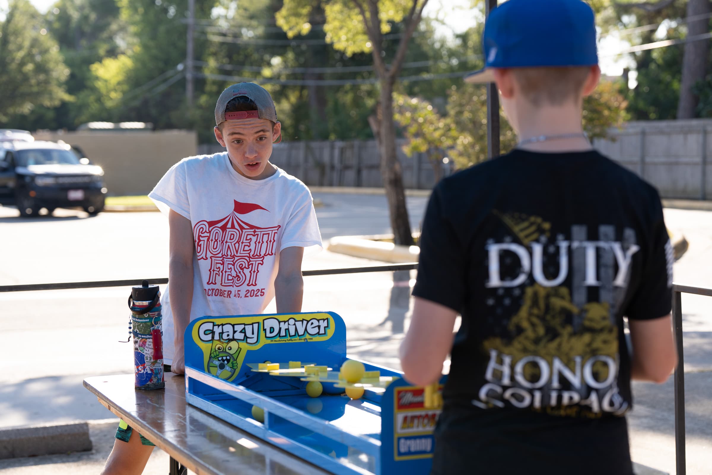 Children playing a colorful outdoor carnival game at a community festival with tents and activities in the background.